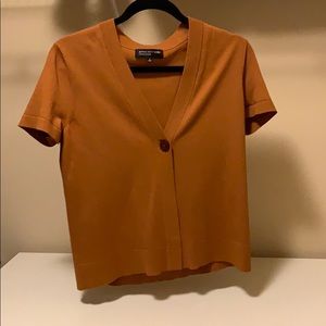 A orange sweater with one wooden button